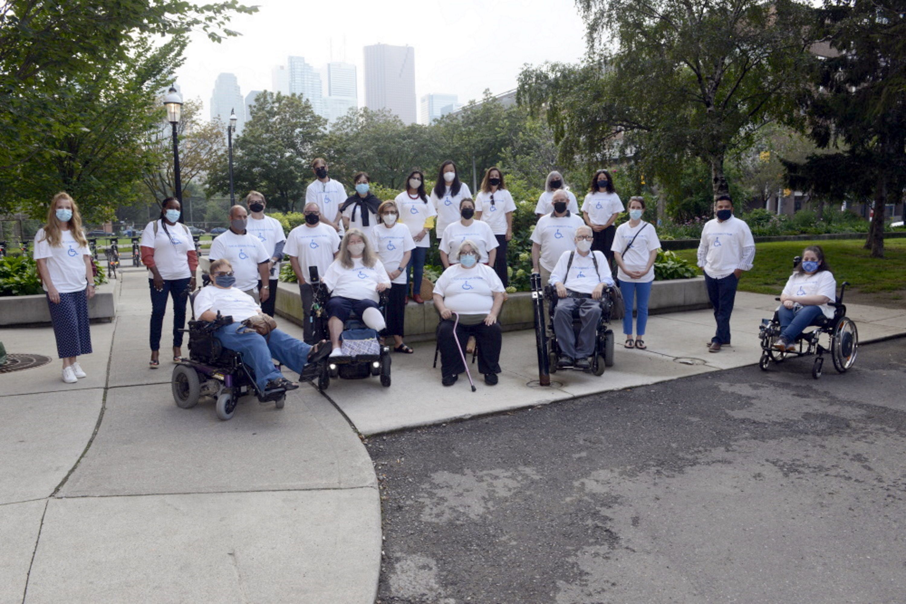 The Accessibility Team wearing white t-shirts with the international symbol for accessibility outside in a park. 