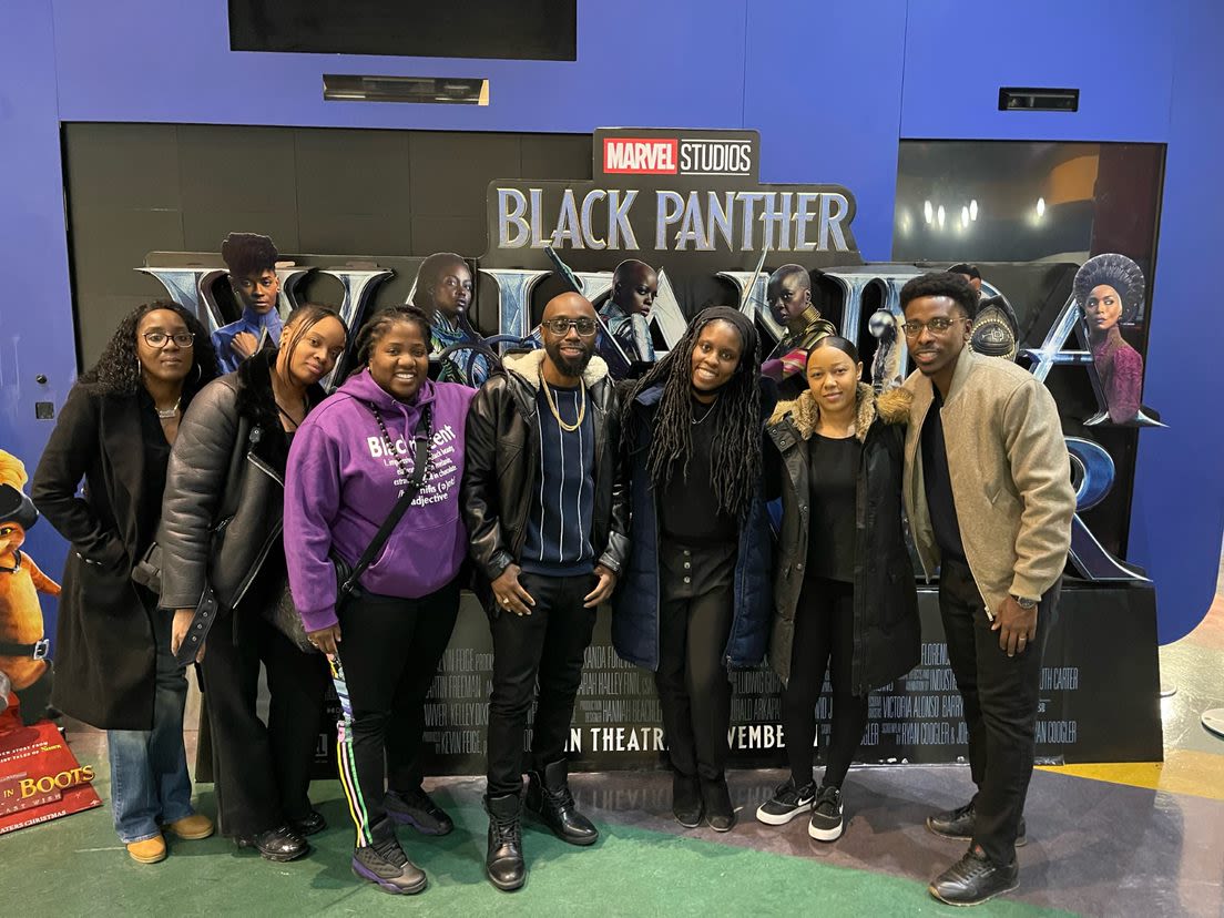 Group of people posing in front of a "Marvel Studios, Black Panther" advertisement
