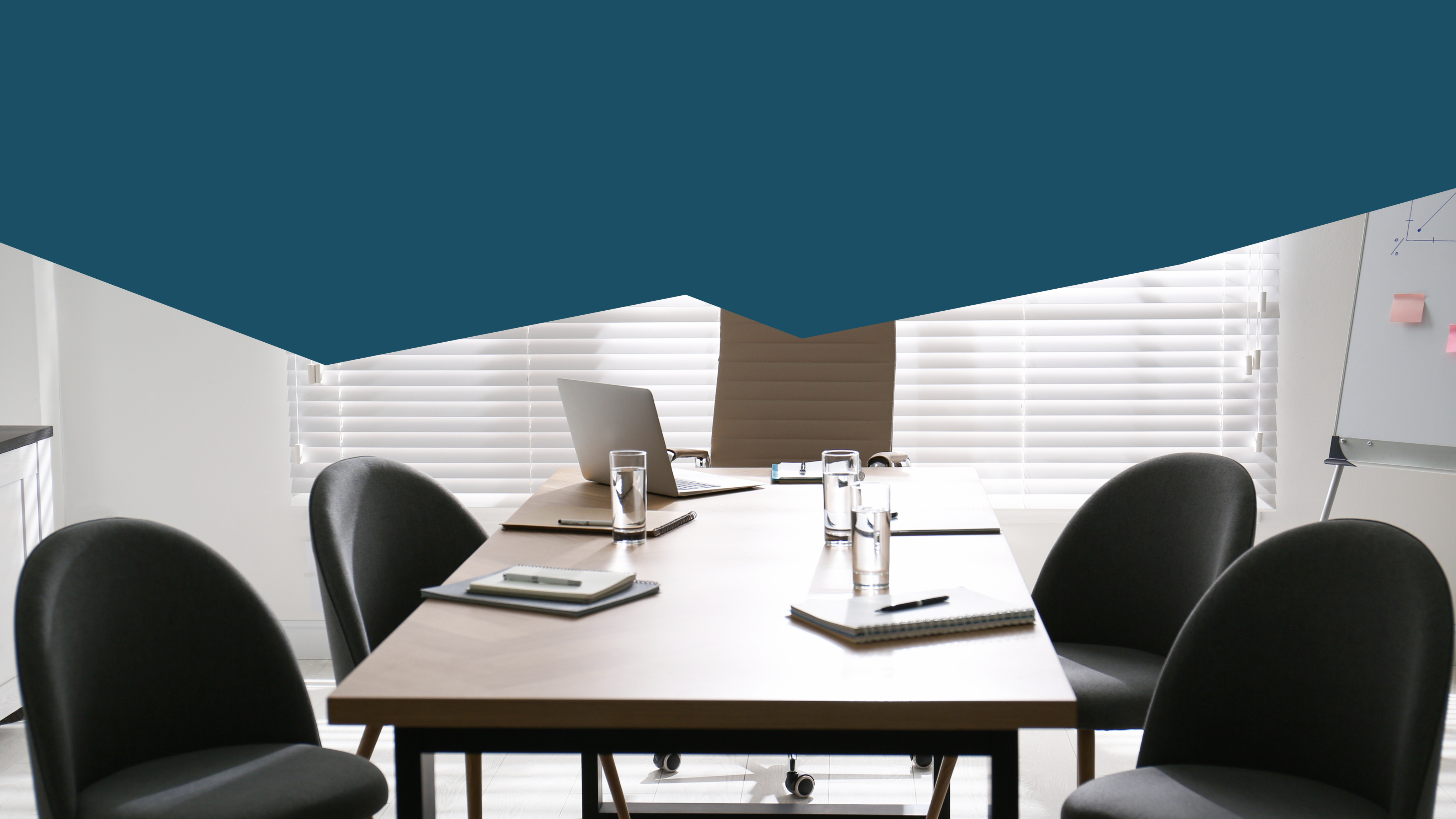 Empty meeting room, black chair surround a table with paper pads and water glasses. There is a whiteboard in the background.