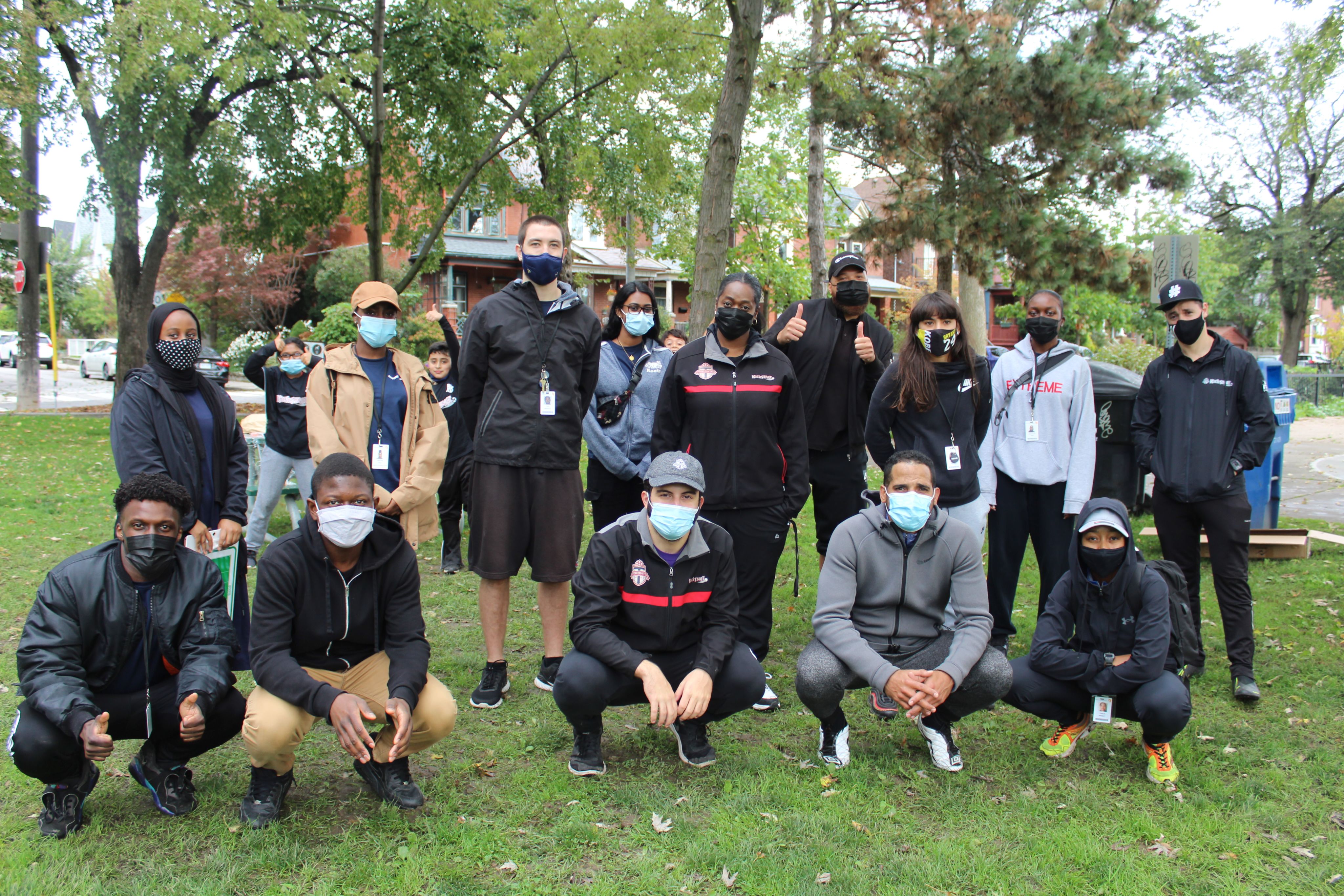 A group of people of various ethnicities wearing face masks posing for the camera in a grassy field.