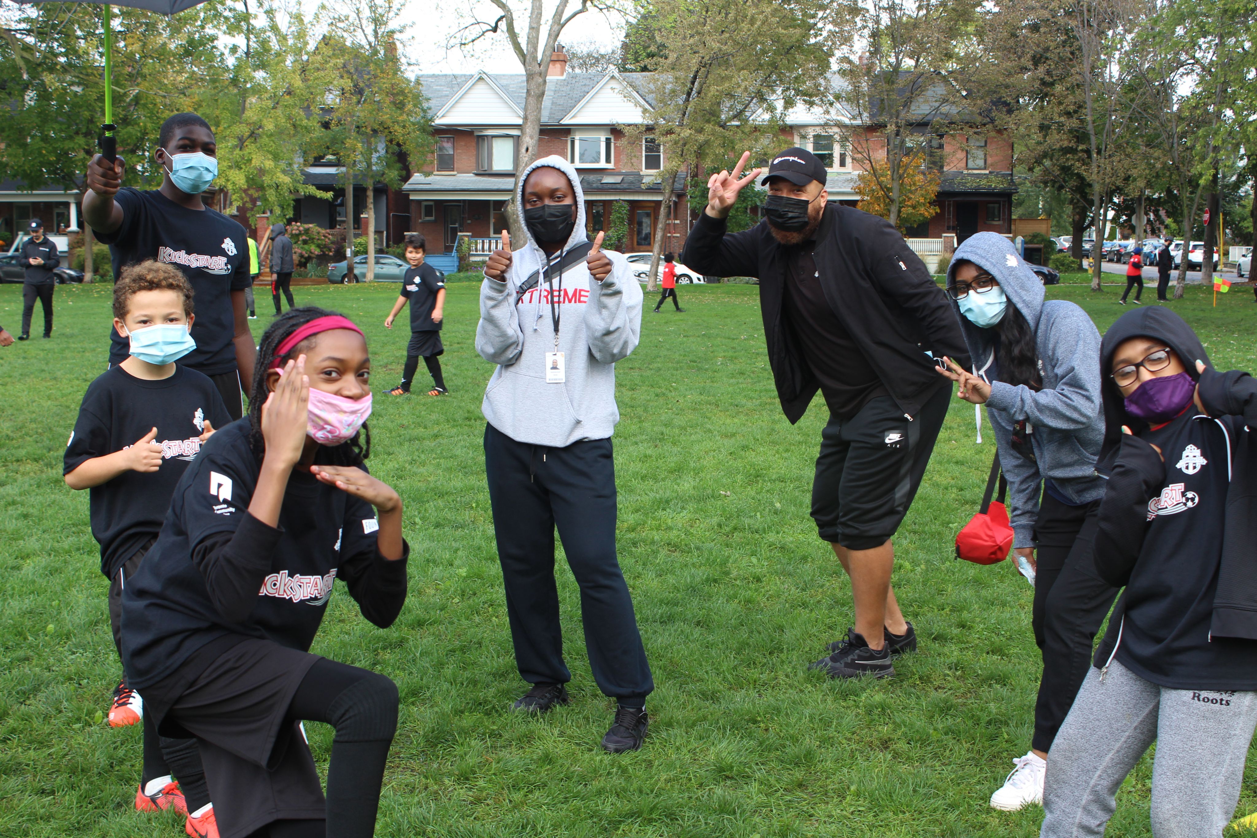 A group of youth wearing face masks posing in front of the camera in a grassy field.
