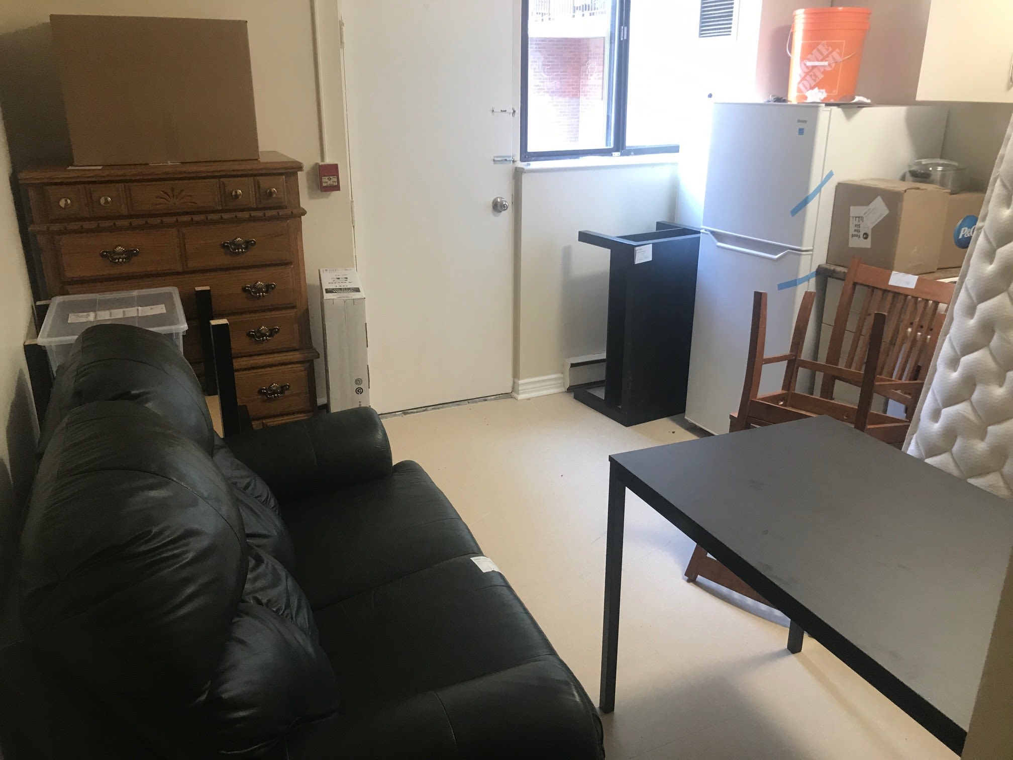 An empty apartment with a black couch, wood dresser, coffee table and assorted other furniture.